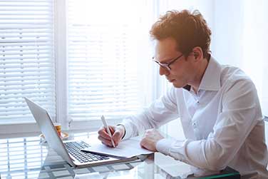 man-writing-and-looking-at-laptop